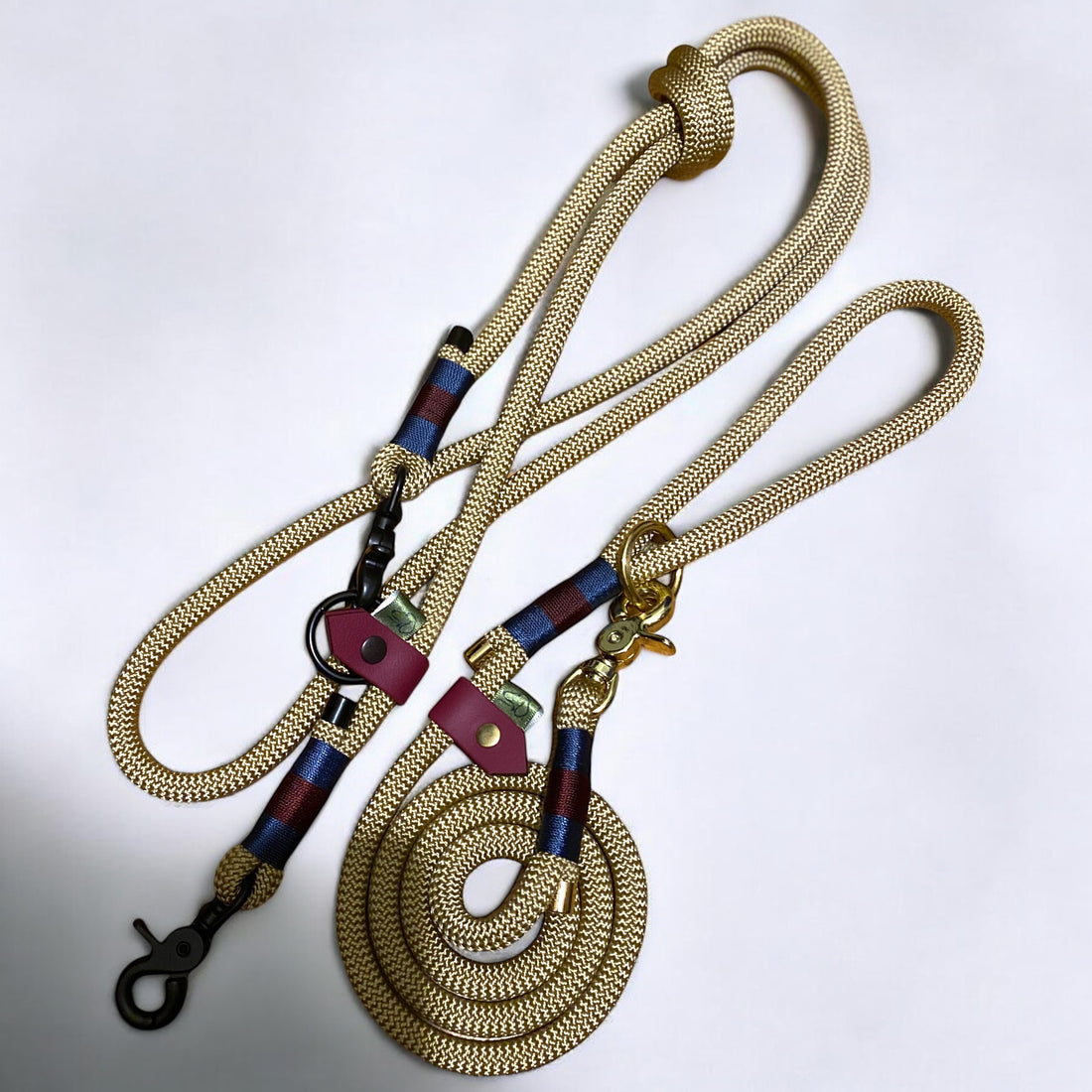 Two Green Dog leads in gold nylon rope with navy blue and maroon Greenwich Yarn binding. One is a regular lead with gold hardware, and the other is a handsfree adjustable lead with black hardware.